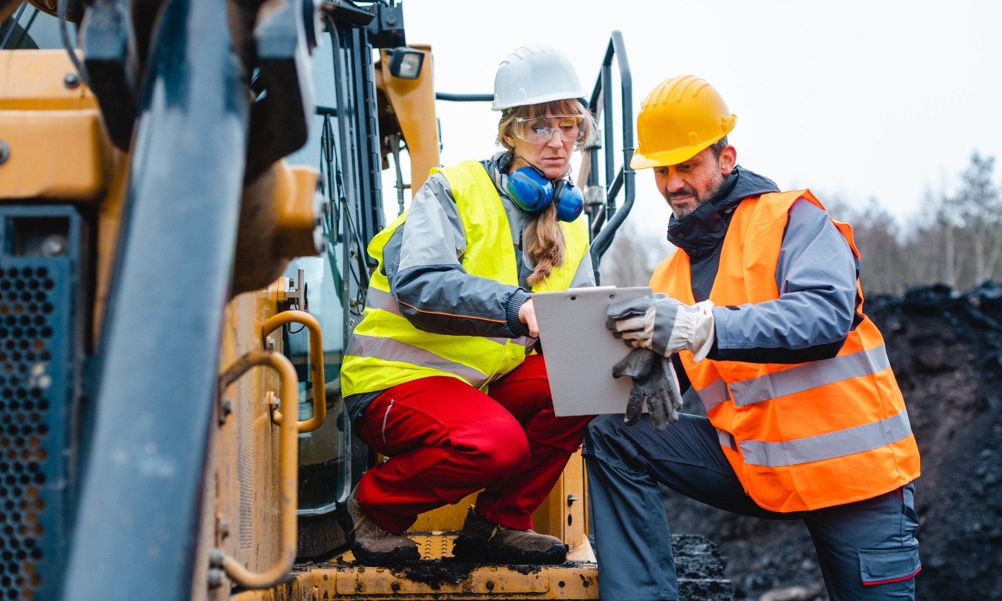Construction workers reviewing site plans on a tablet next to heavy machinery